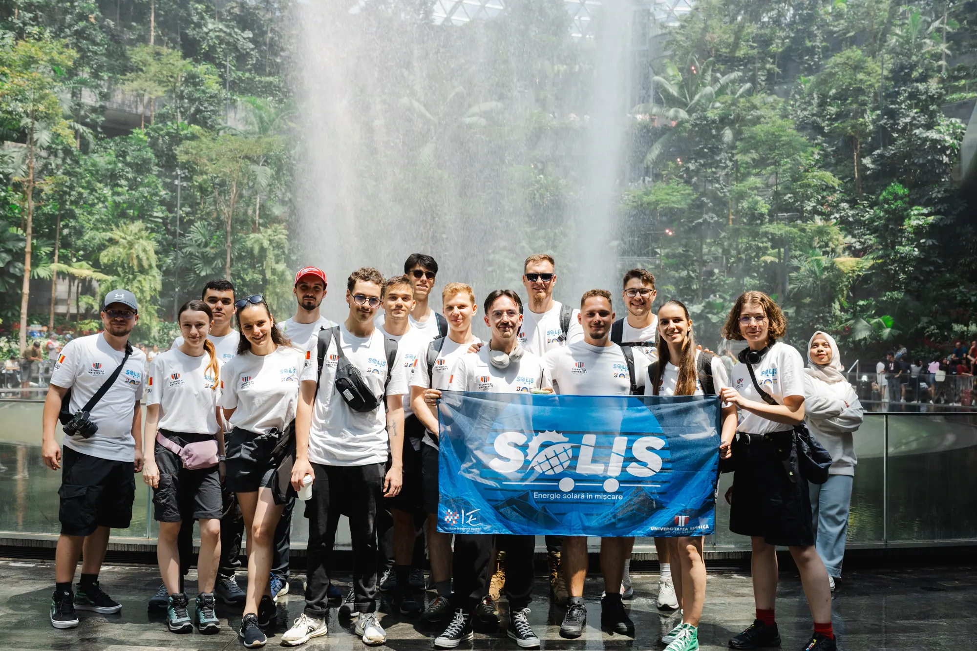 Membri ai echipei Solis cu bannerul SOLIS în fața unei cascade interioare, în drum spre Australia, în 2025