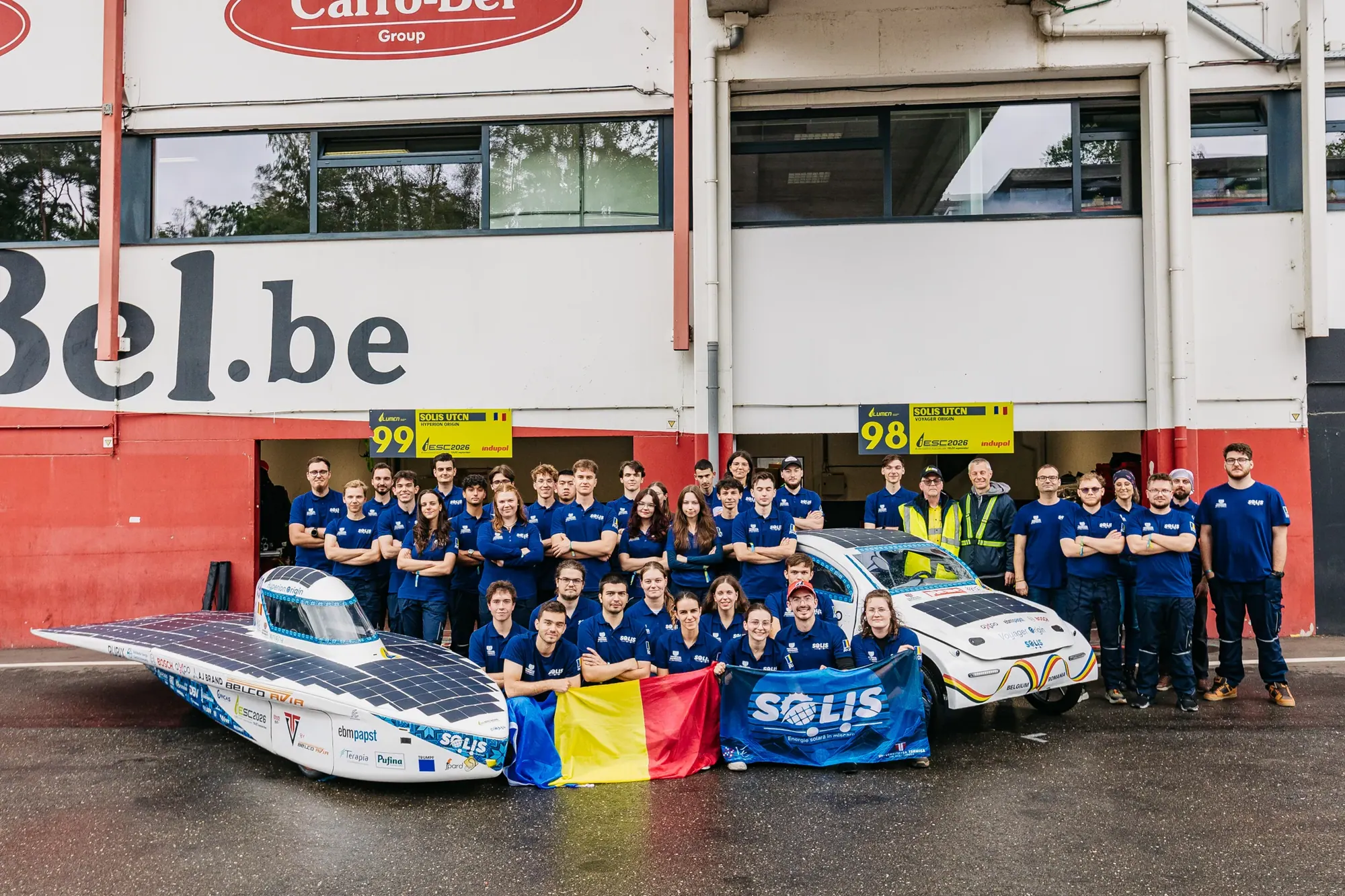 Toată echipa cu ambele vehicule și steagul României în fața garajelor de la Zolder.